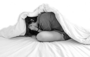 girl suffering from anxiety covering her face under the covers